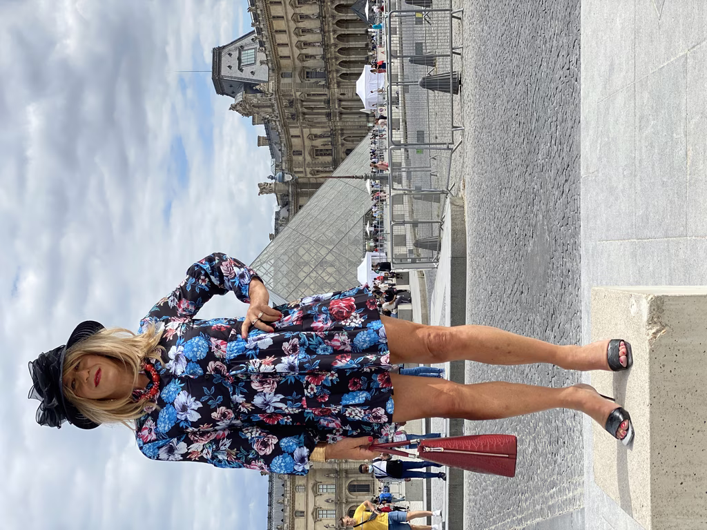 Dans l'ombre grandiose du Louvre, Déborah se tient avec une assurance tranquille. Sa robe florale est une célébration de sa féminité, et son chapeau un clin d'œil audacieux à la mode parisienne. Elle incarne l'esprit de ceux qui n'ont pas peur d'affirmer leur identité en public, offrant une inspiration vivante à la communauté transgenre et travestie. Le cadre historique et sa silhouette élégante sont un puissant rappel que l'authenticité est une forme d'art en soi