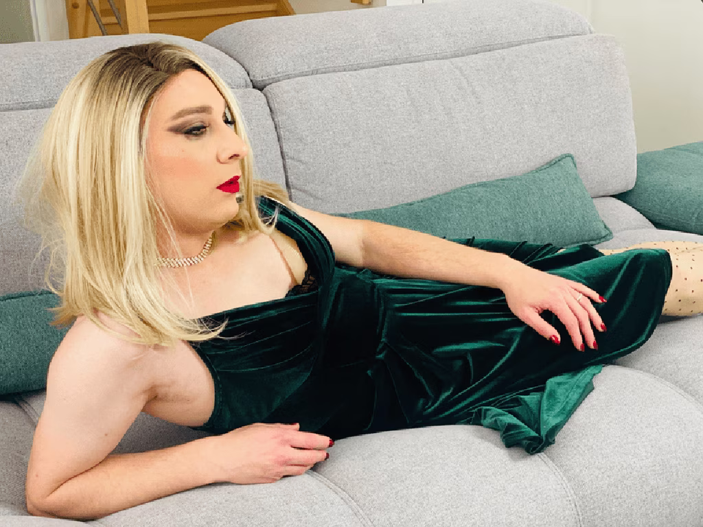 Stella allongée sur un canapé, portant une robe en velours vert, dans un salon éclairé