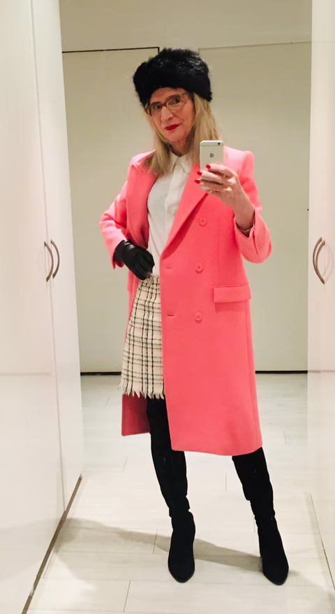 Claude posant avec un manteau rose vif, des bottes noires et un accessoire en fausse fourrure, parfaite inspiration pour un look hivernal féminin et élégant