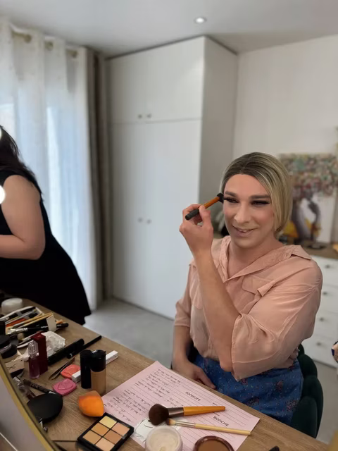 Stella est en pleine transformation chez Transbeauté, appliquant elle-même du maquillage sous les conseils de Jennifer, la maquilleuse professionnelle. Sa compagne, visible en arrière-plan, est présente pour la soutenir. Ce moment intime et révélateur permet à Stella de se féminiser avec assurance et plaisir. Assise devant une coiffeuse chargée de produits de beauté, Stella sourit, reflétant la joie de découvrir et d'embrasser son identité féminine. L'atmosphère lumineuse et accueillante du salon ajoute à la sérénité et à la beauté de ce moment précieux partagé avec sa compagne
