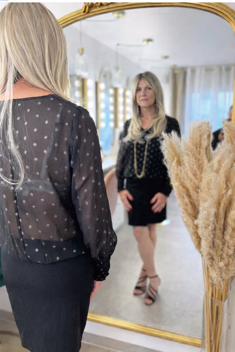 Femme transgenre ou travestie affirmée face à son reflet, symbole de féminisation réussie, de confiance retrouvée et de l’accompagnement bienveillant proposé par Transbeauté