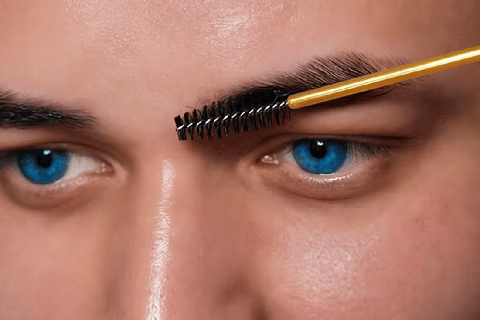 Gros plan sur un brossage de sourcils avec goupillon – préparation essentielle avant l'épilation ou le brow lift pour une mise en beauté transgenre précise.