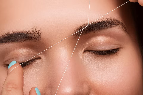 Gros plan sur une épilation des sourcils au fil sur paupières fermées – méthode précise et naturelle pour sublimer le regard des femmes transgenres.