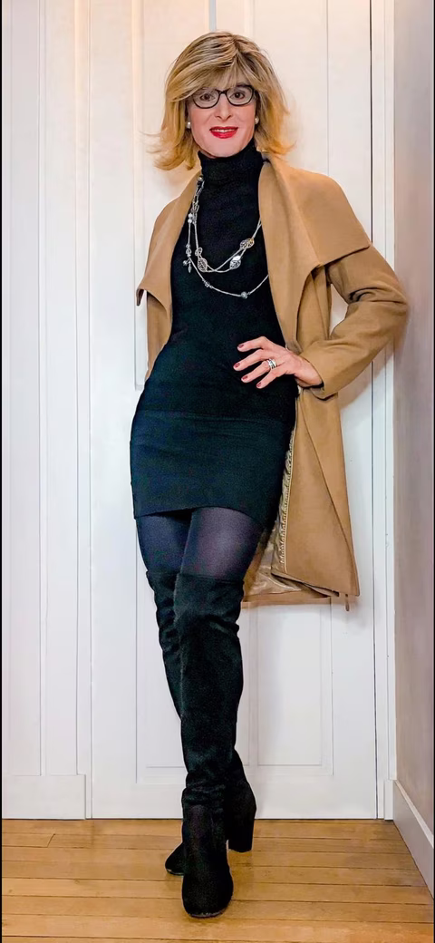 Glawdys posant avec élégance dans une tenue hivernale chic, composée d'un manteau camel, une robe noire et des bottes hautes, incarnant la féminité moderne.