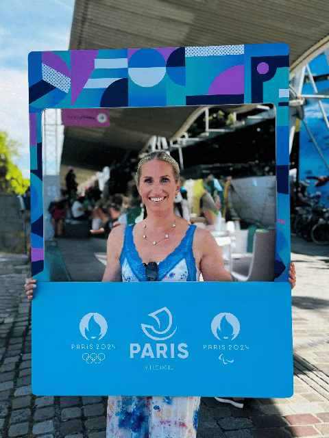 Jennifer de chez Transbeauté tient un cadre promotionnel de Paris 2024 lors d'un événement lié aux Jeux Olympiques et Paralympiques. La visibilité et l'inclusion des personnes LGBT aux Jeux de Paris 2024 soulignent l'engagement pour des Jeux ouverts, respectueux de la diversité et des droits humains