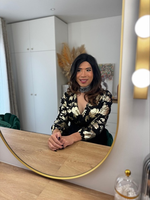 Sarah, travesti accompagnée par Transbeauté, pose dans le miroir du studio après sa séance de maquillage, en tenue féminine noire fleurie, avant sa première sortie shopping