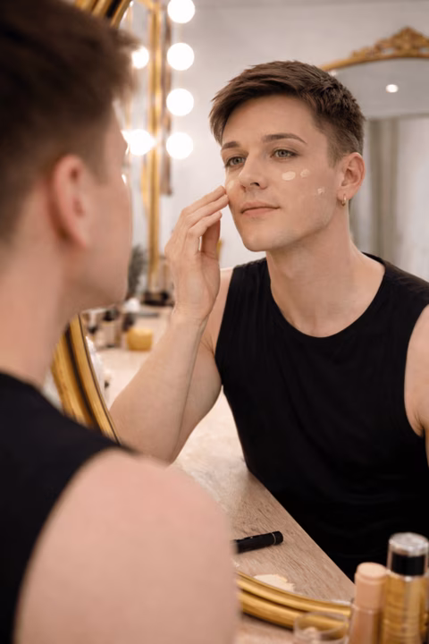 Homme appliquant du fond de teint pour cacher l’ombre de la barbe devant un miroir dans le studio Transbeauté